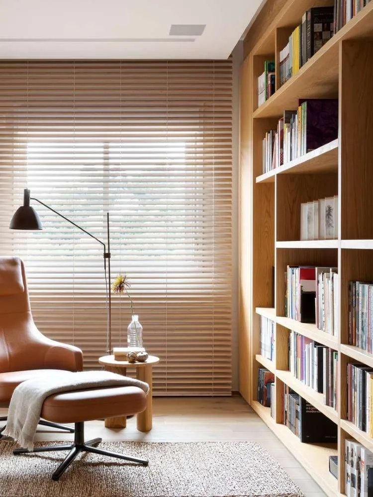 Cantinho da leitura com poltrona grande e marrom, luminária de chão e iluminação natural da janela. 