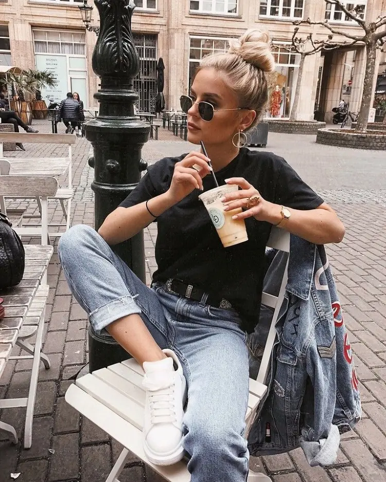 Frase para foto pensativa mulher loira com coque sentada toma café usa óculos de sol e veste calça jeans, cinto preto e t-shirt preta Frase para foto pensativa
