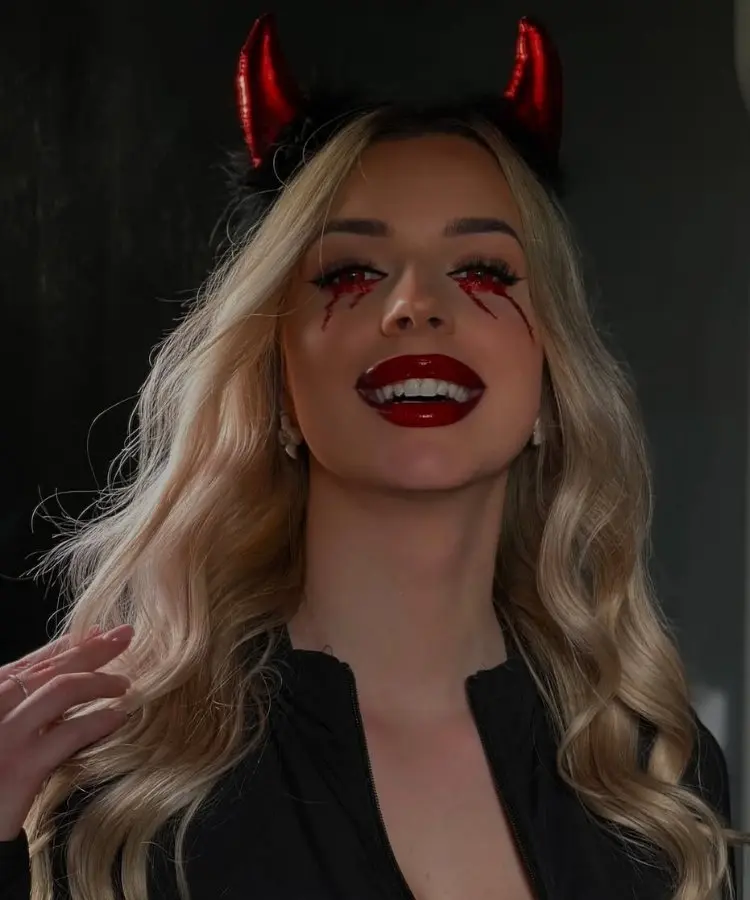 Foto de mulher loira usando maquiagem de diaba com olhos com sangue de glitter
