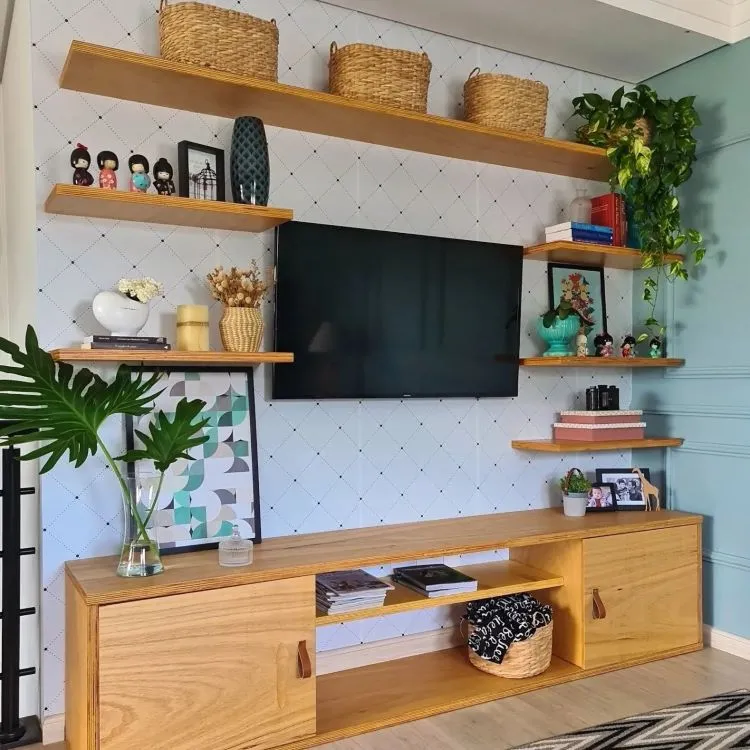 Sala de estar com rack de madeira, televisão, quadros na estante, diversos itens decorativos e vaso com jiboia na prateleira superior.