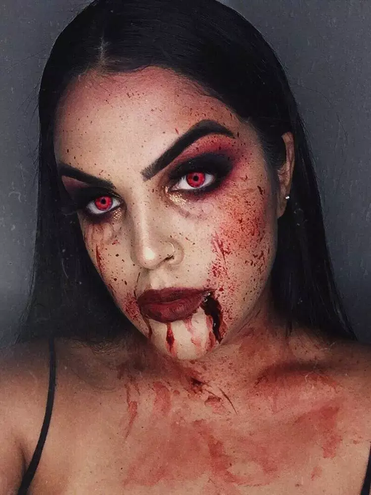 Mulher de pele clara usando maquiagem vermelha e preta nos olhos, batom vermelho e sangue por todo o rosto