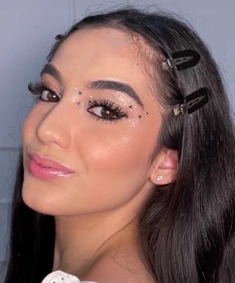 Mulher de pele clara com maquiagem glossy nos olhos  com estrelas