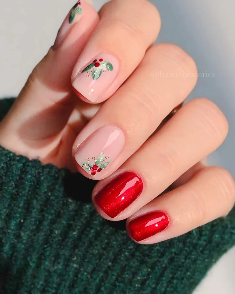 Mão com unhas curtas decoradas para Natal em vermelho brilhante, nude e desenho de planta azedinha