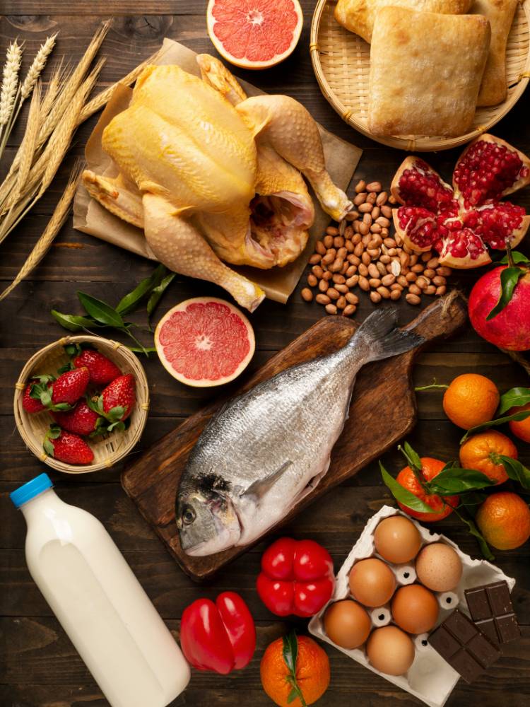 Mesa com alimentos como peixe, frango, morango, laranja, tomate, leite e ovos