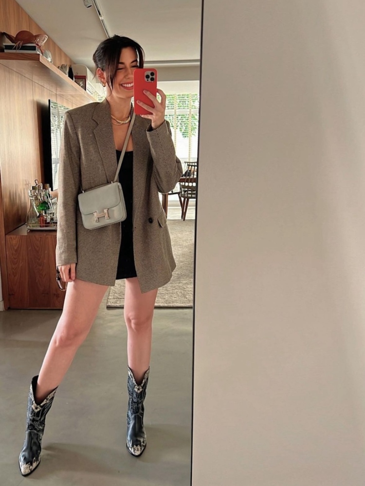 mulher usando vestido preto com blazer cinza por cima com bota estilo western preta e bolsa transversal