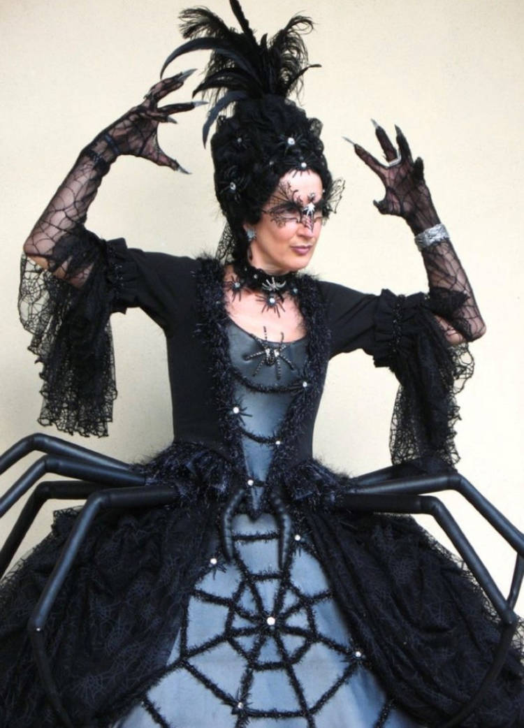 Mulher de pele clara com fantasia medieval de aranha, com vestido elaborado, luvas de teia e máscara 
