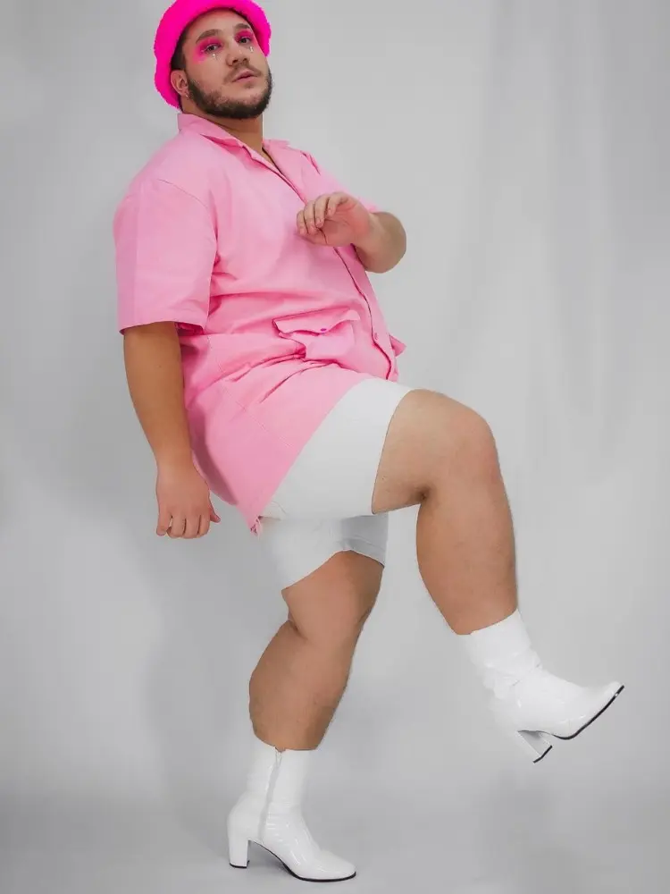 Homem de pele clara usando camisa rosa, bermuda branca, bota cano baixo e bico fino branca