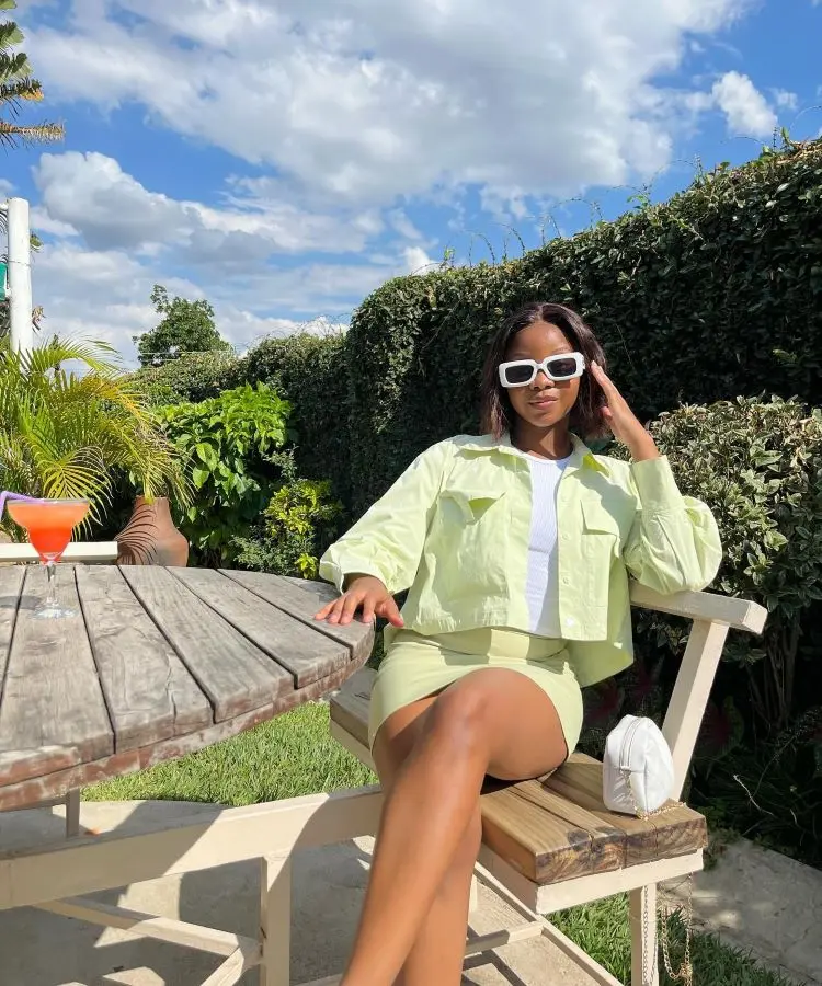 Menina com conjuntinho de jaqueta e saia na cor verde-claro, sentada em mesa de madeira
