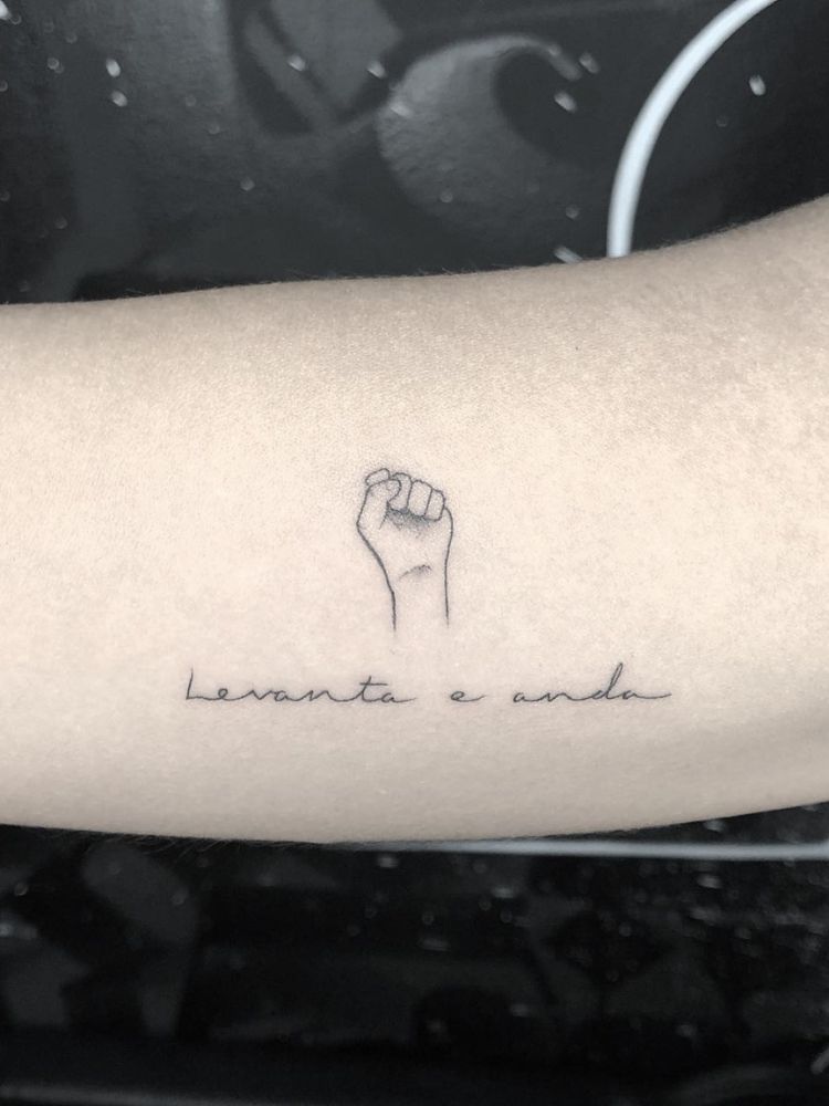 Braço com punho tatuado e frase"levanta e anda"