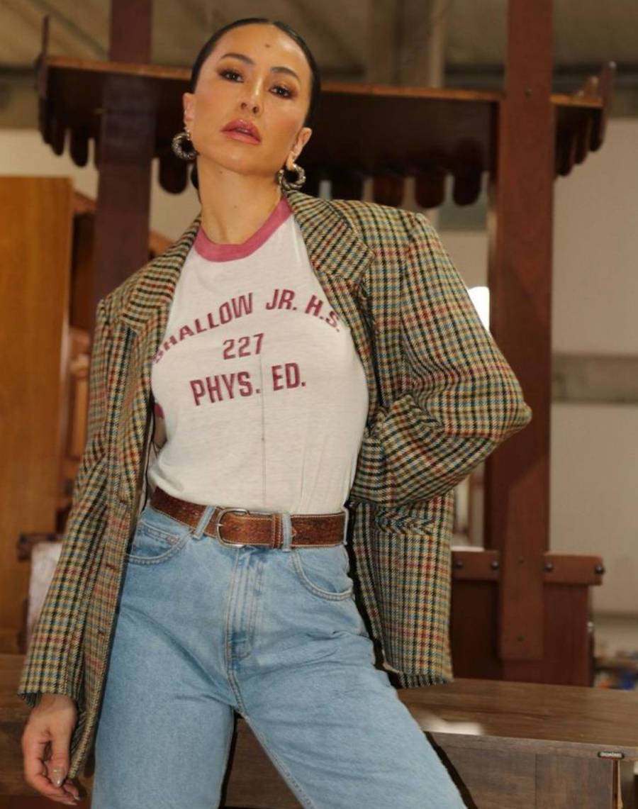 Imagem de Sabrina Sato usando im blazer xadrez, uma camisa básica com escritas vermelhas em inglês, uma calça jeans e um cinto marrom