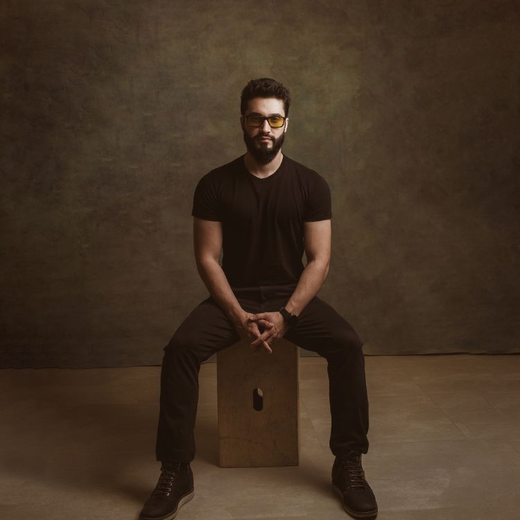 Alan Nicolas, homem de pele clara usando blusa e calça pretas, sentado