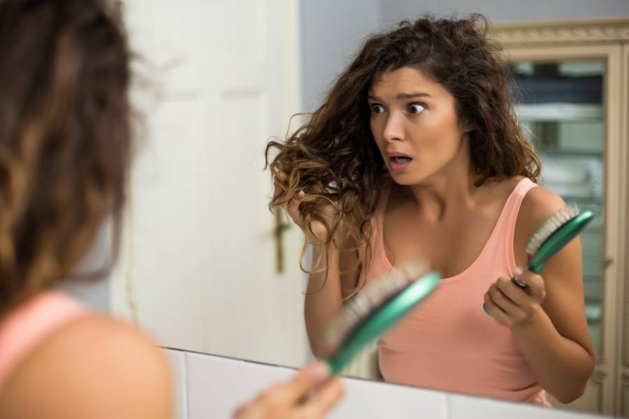 Mulher assustada se olhando no espelho e segurando o cabelo.
