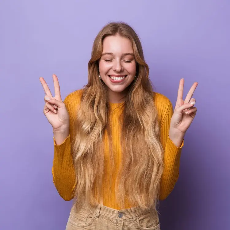 Mulher loira de pele clara em fundo roxo usando blusa laranja e calça bege