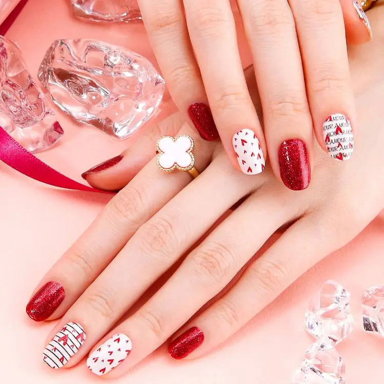 mãos de pele clara com unhas curtas redondas com esmalte vermelho; esmalte branco com corações