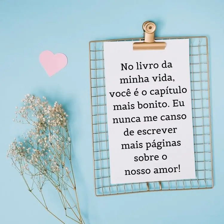 Foto de fundo azul com flores secas e mural com página branca escrito " No livro da minha vida, você é o capítulo mais bonito. Eu nunca me canso de escrever mais páginas sobre o nosso amor!"