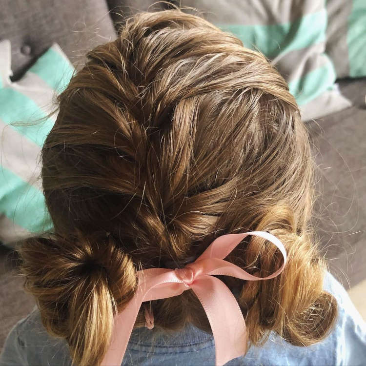 Dois coques em cabelo castanho com um fita rosa formando um laço.