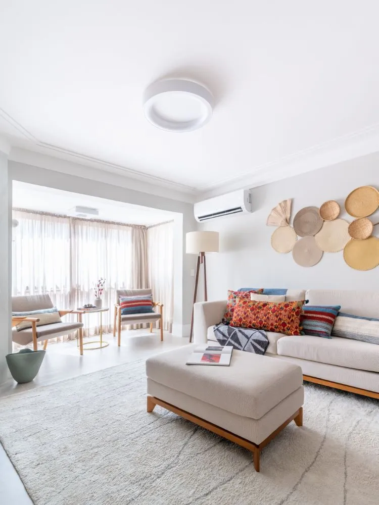 Sala de estar com cores neutras, decorações circulares em tons terrosos na parede e uma enorme porta de varanda coberta por uma cortina fina.