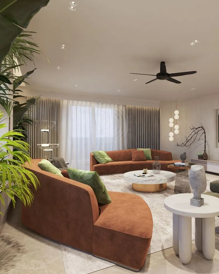 As paredes são brancas, o sofá é marrom, as almofadas são uma mistura de verde e marrom, com decorações cinza e cortinas cinza. Algumas plantas adicionam toques de verde.