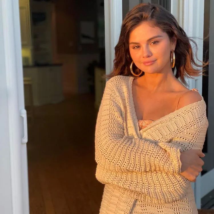Foto de Selena Gomez usando um suéter e brincos de argola com cabelo médio ao vento 