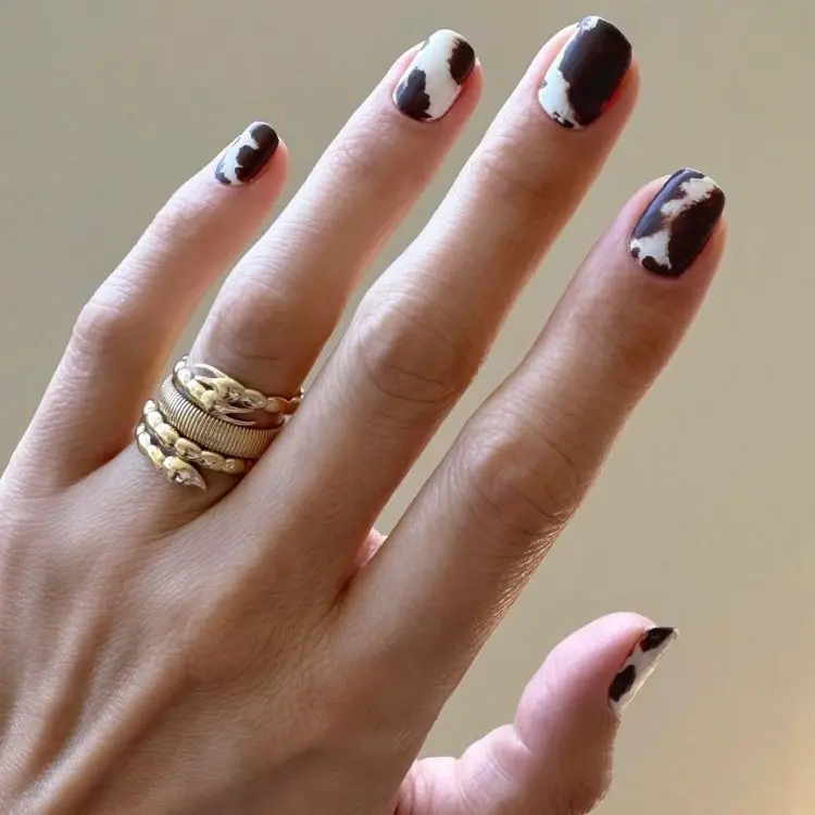 Mão com unhas curtas arredondas com nails alrt de vaca branca e marrom 