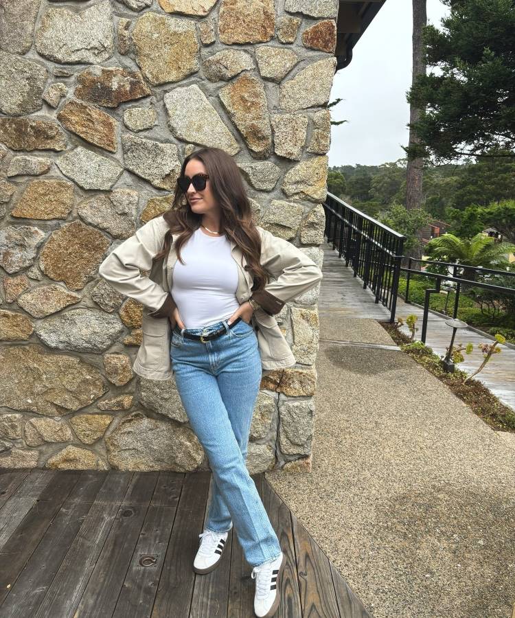 A imagem mostra uma mulher usando um jeans skinny de lavagem clara, tendência para 2025. O corte clássico e ajustado combina com tênis branco e um cinto preto, criando um look casual e moderno, perfeito para o dia a dia.