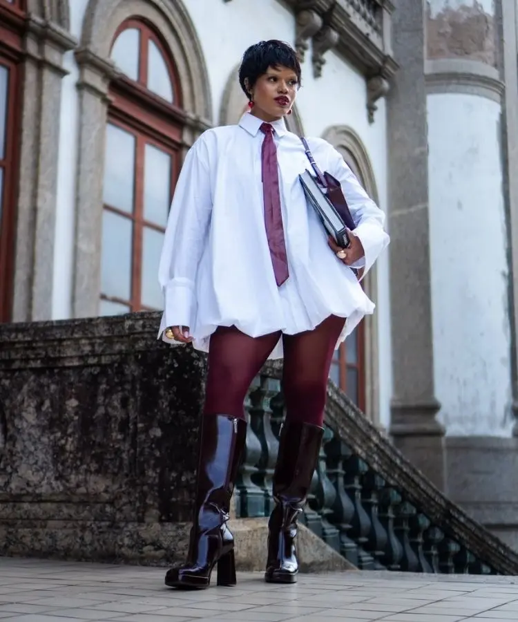 Foto de Josy Ramos, uma das influenciadoras negras de moda, usando camisa branca com gravata, meia e bota bordô