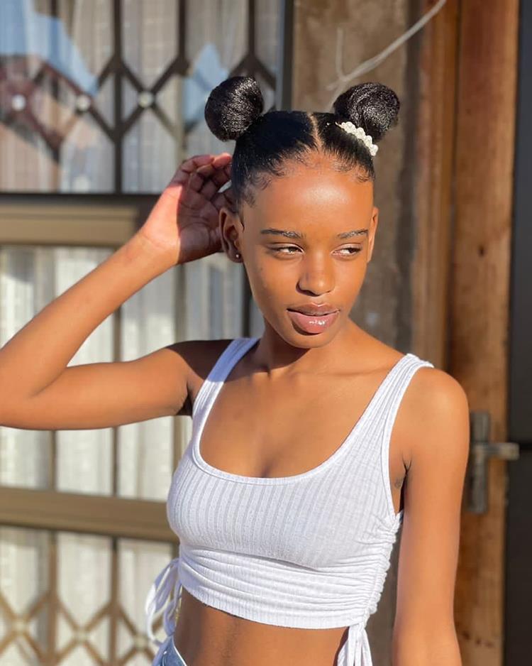 Menina de pele negra com top branco, shorts heans e space buns no cabelo preto 