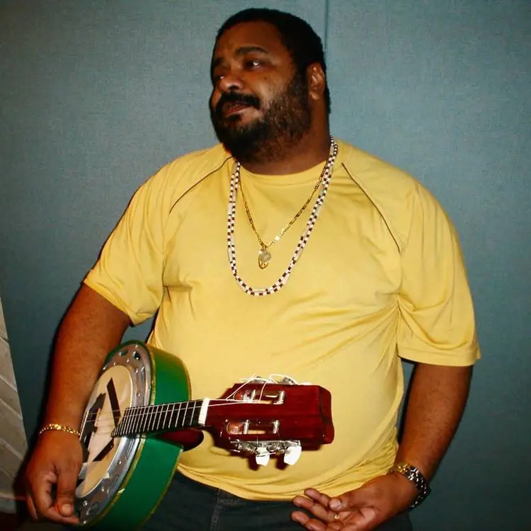 Sambista quando era mais novo, usando camisa amarela e segurando cavaquinho