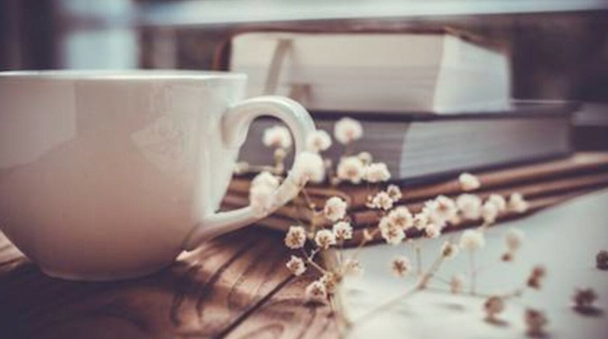 Foto de livros empilhados atrás de xícara branca e flores