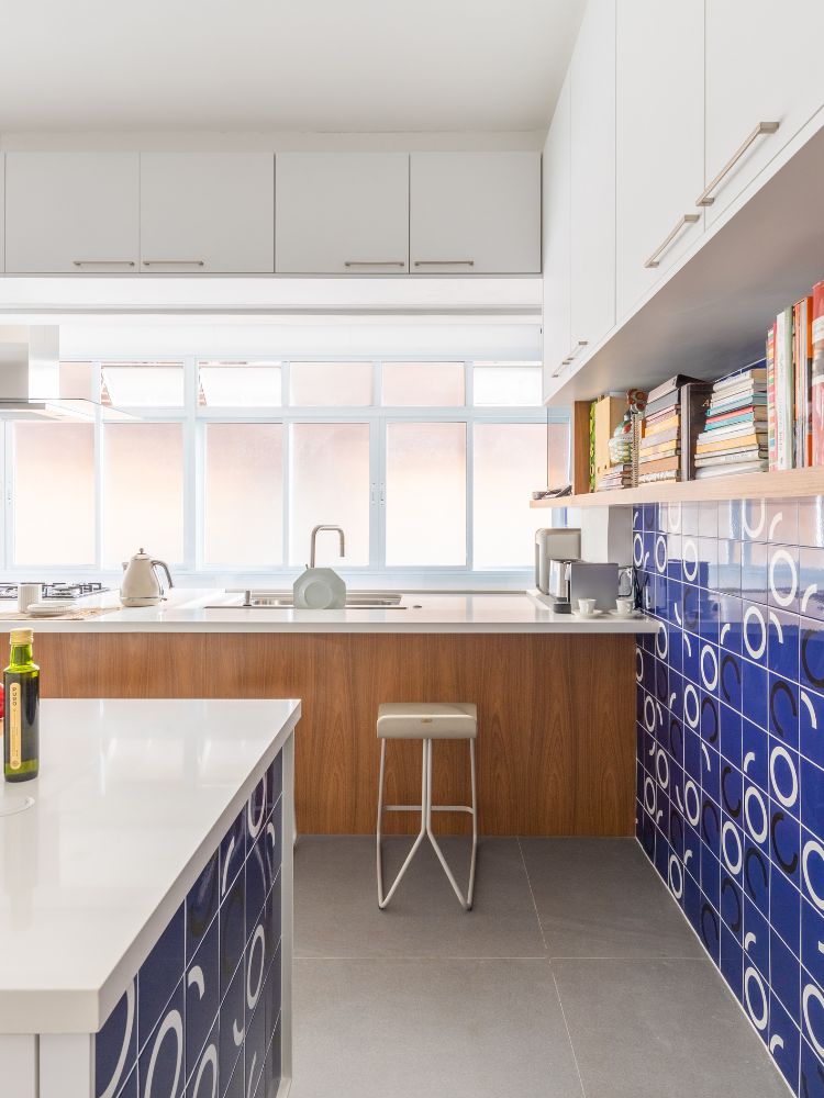 Cozinha com azulejos azuis, móveis brancos e bancada de madeira 