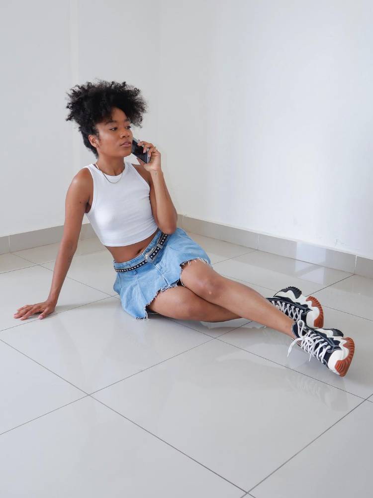 mulher usando regata branca com saia jeans de pregas e All Star preto
