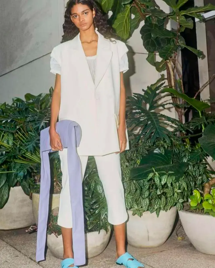 Modelo com terno de verão branco e bolsa roxa.