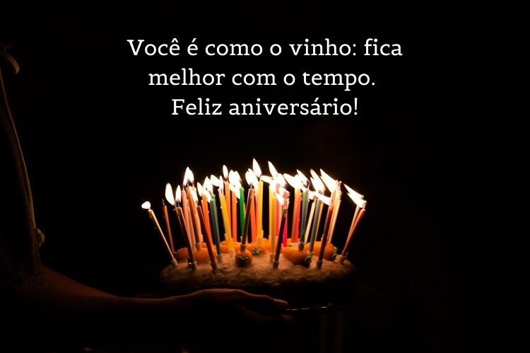 Fundo preto com pessoa conduzindo bolo cheio de velas coloridas e frase " Você é como o vinho: fica melhor com o tempo. Feliz aniversário!"