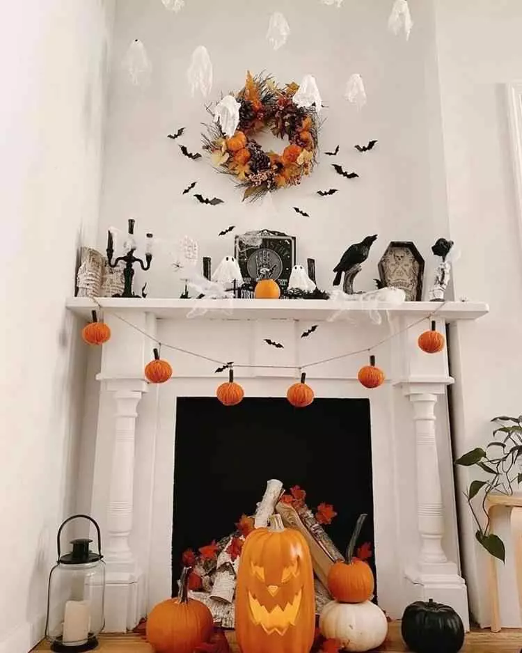lareira decorada para dia das bruxas, com abóboras ao redor, fantasmas pequenos, morcegos de papel, teias, corvo e mais