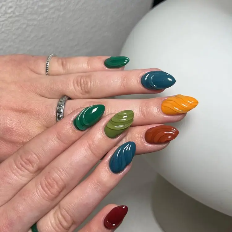 Mãos de pele clara com unha stiletto em verde, azul, marrom e vinho com textura em linhas 