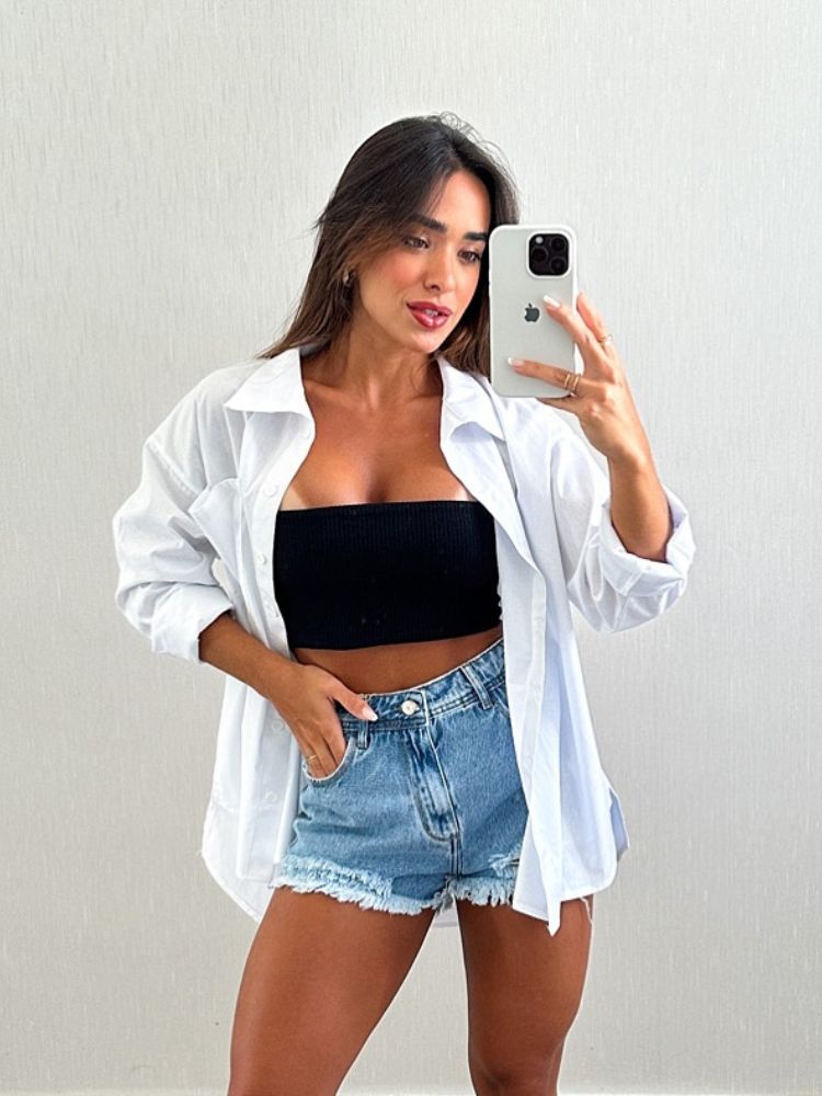 Mulher de pele clara bronzeada usando shorts jeans, top preto e camisa branca