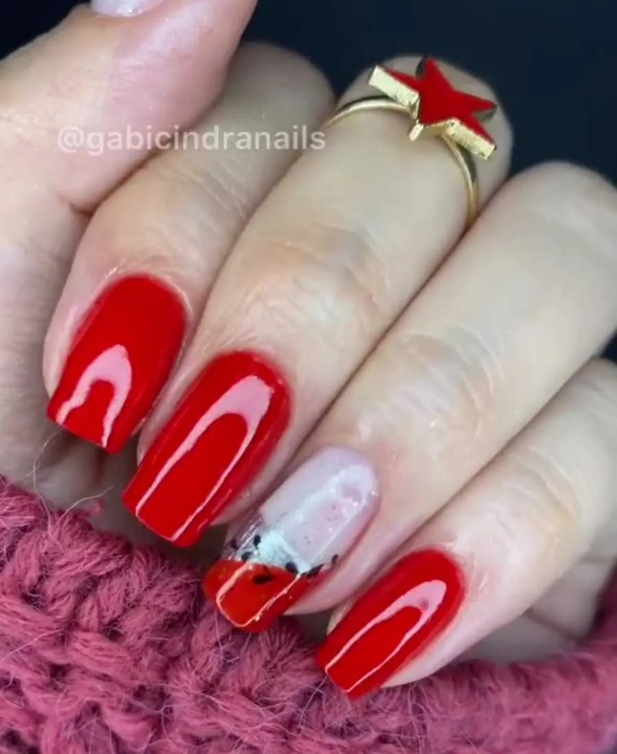 Mão de pele clara com unhas quadradas em vermelho e anelar com vermelho, prata e adesivo