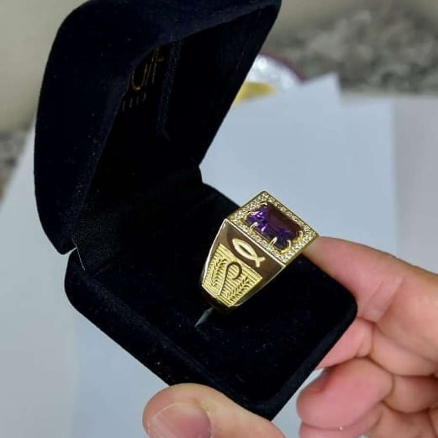 Anel dourado com pedra roxa em caixa preta