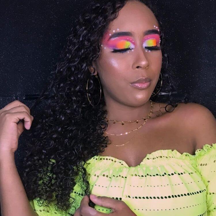 Mulher de pele negra usando maquiagem neon colorida nos olhos e strass imitando pérola