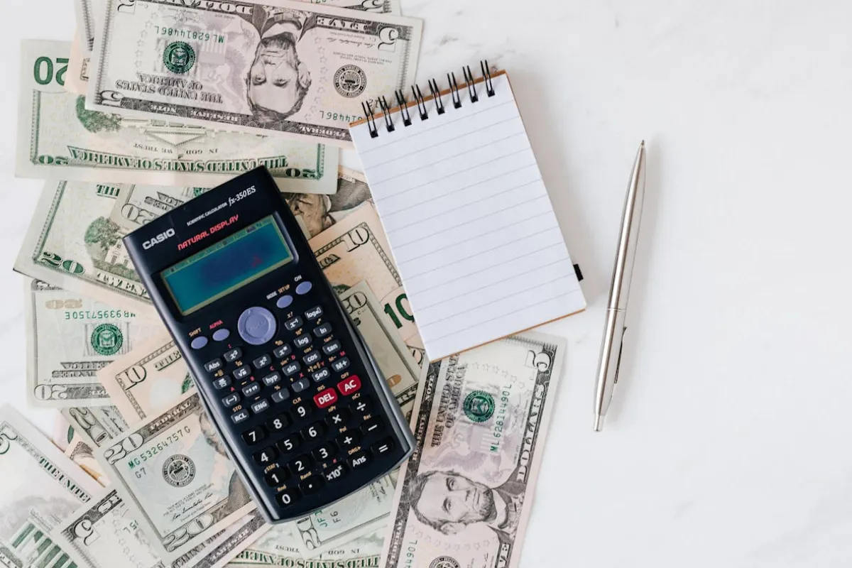 Mesa com calculadora, caderno, caneta e cédulas espalhadas