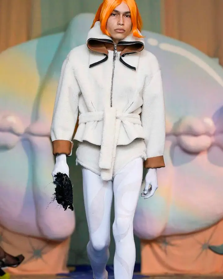 Modelo com peruca laranja usa legging branca e casaco felpudo também branco.