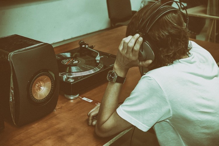 Homem de pele clara usando blusa branca, ouvindo música em disco de vinil 