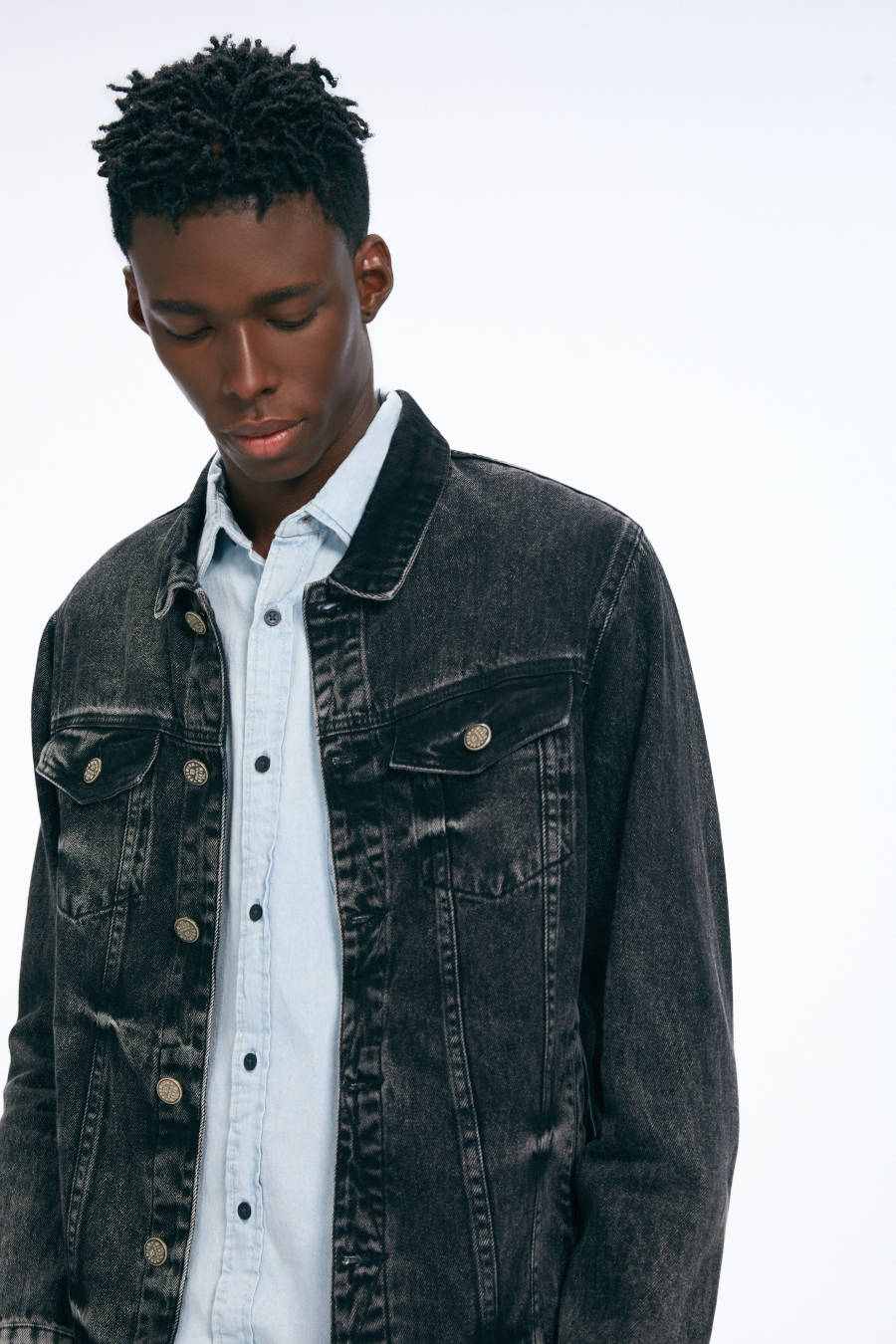 Imagem de homem olhando para baixo e vestindo jaqueta jeans preta, composta com uma blusa social azul e jeans por baixo