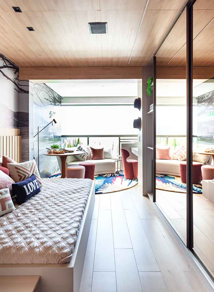 foto de quarto integrado com varanda, com armário com espelhos, cama com almofadas, sofá bege na varanda e puffes rosas