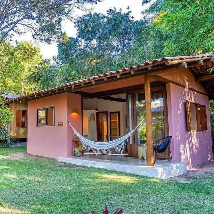 entrada de lar rosa, com varanda e rede de rnda branca, ao redor de árvores