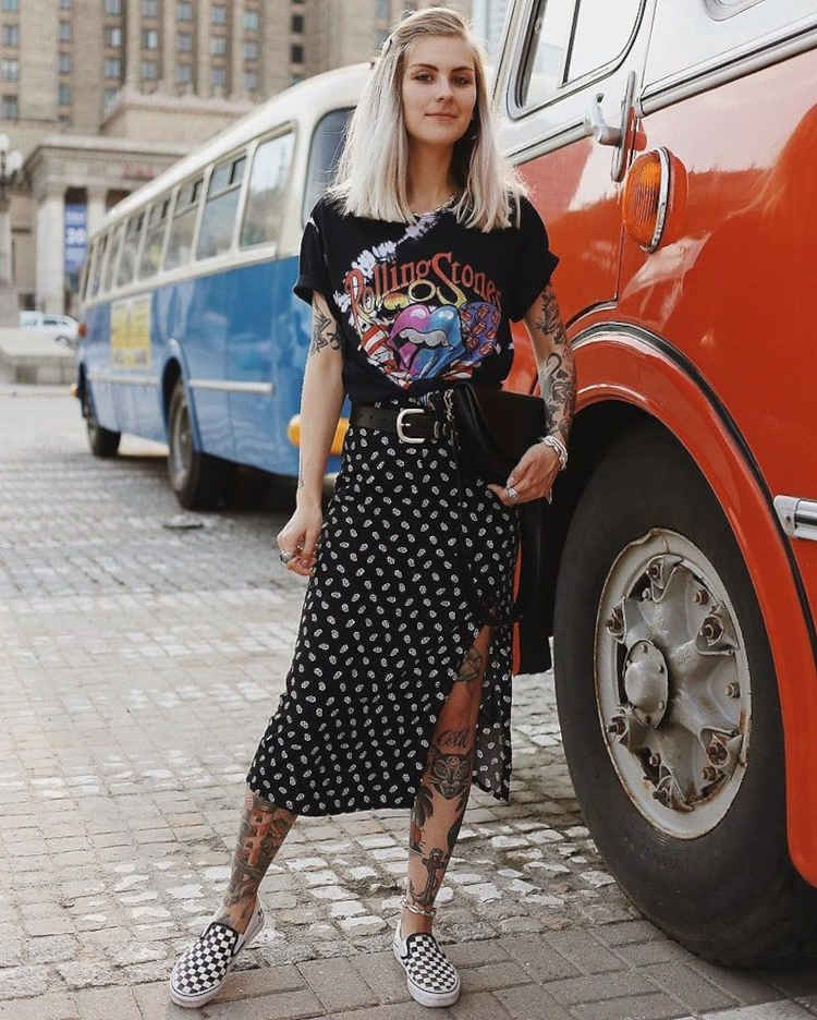 Mulher loira tatuada usando camisa preta de banda e saia midi preta e branca