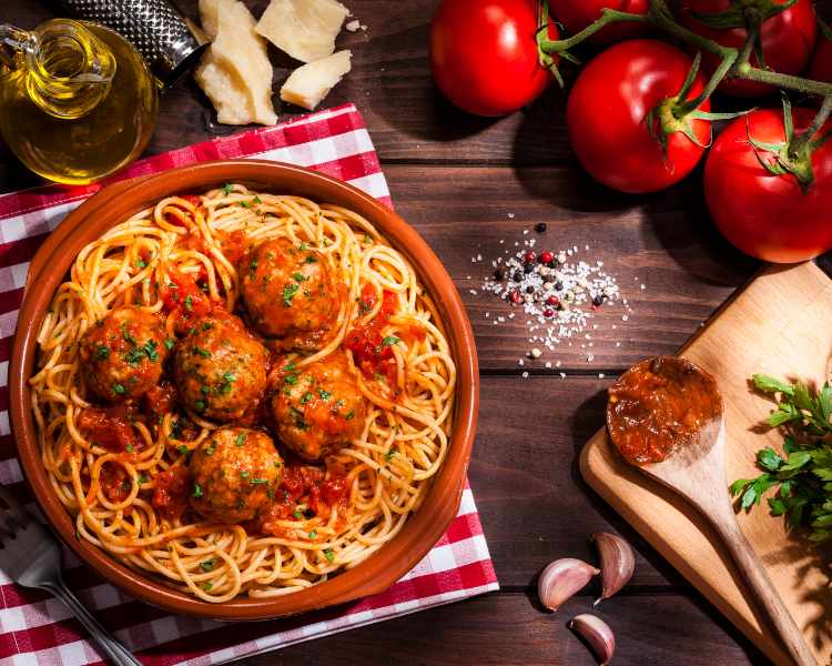 Macarrão com almôndegas em mesa com tomates, azeira, queijo, etc