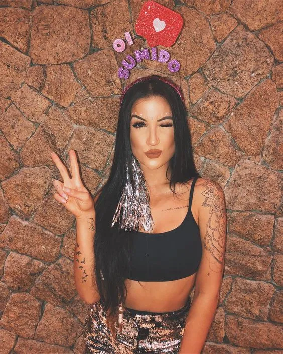 Boca rosa de cropped preto e shorts metalizado, além de tiara "Oi sumido"