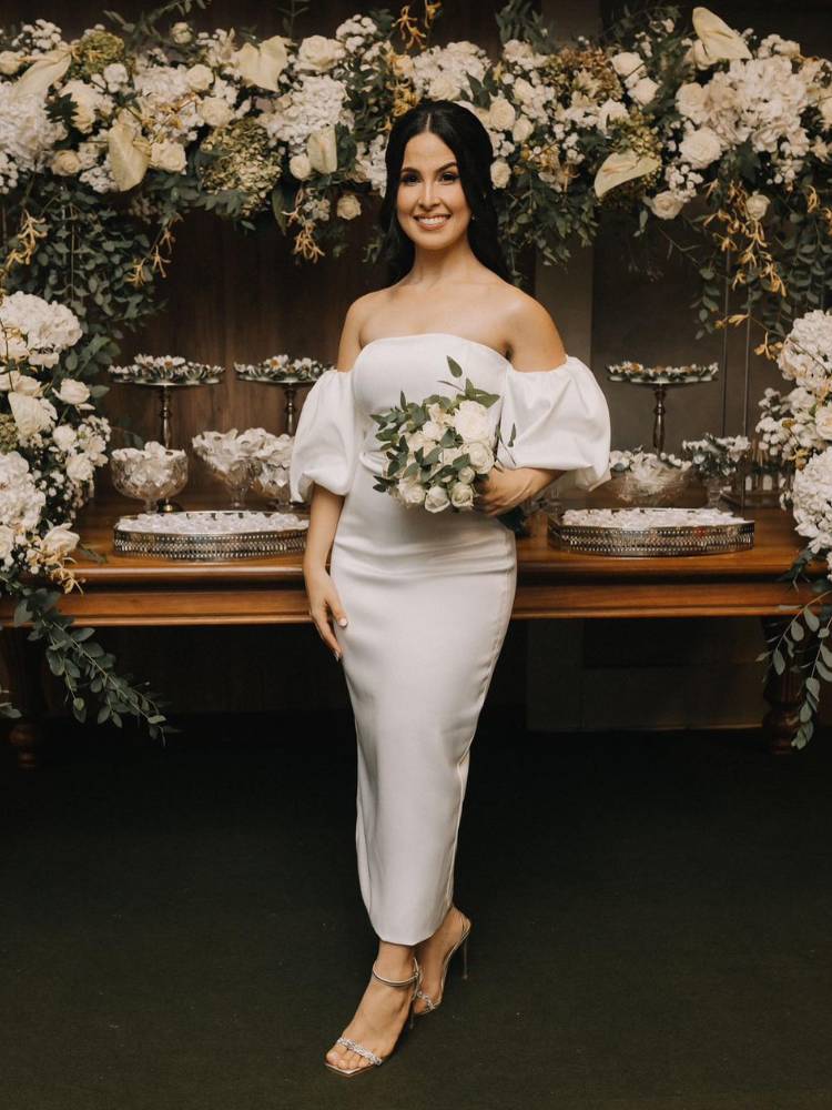 Mulher de pele clara usando vestido de noiva curto e monimalista, sem bordados, com manga bufante removível e segurando buquê