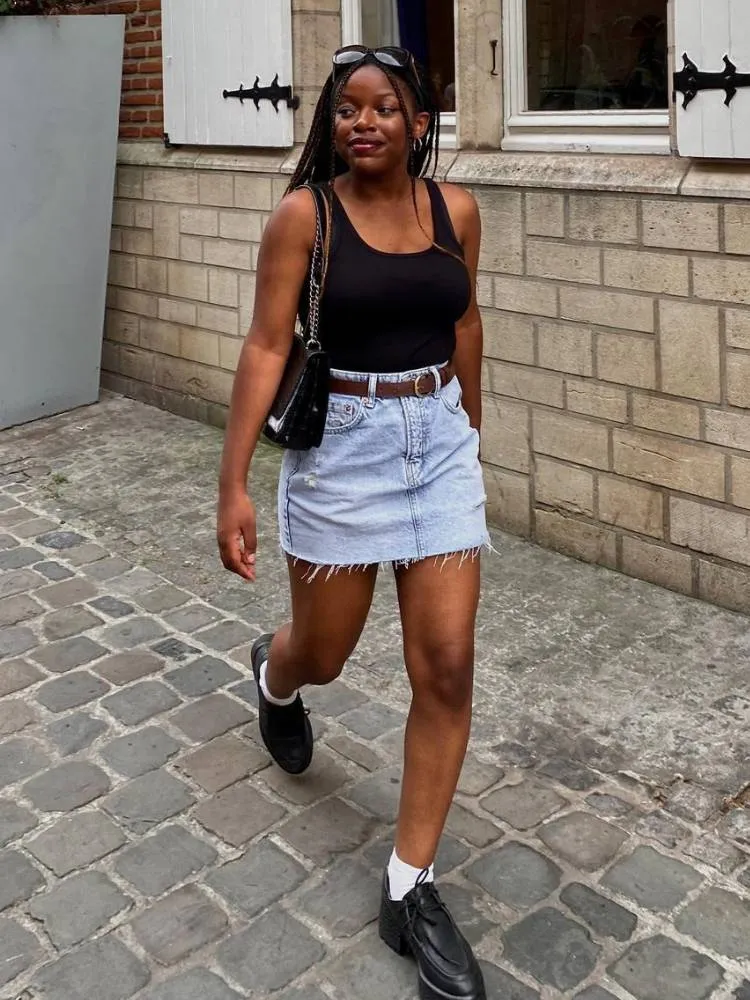 mulher usando regata preta, saia jeans e mocassim com meia branca